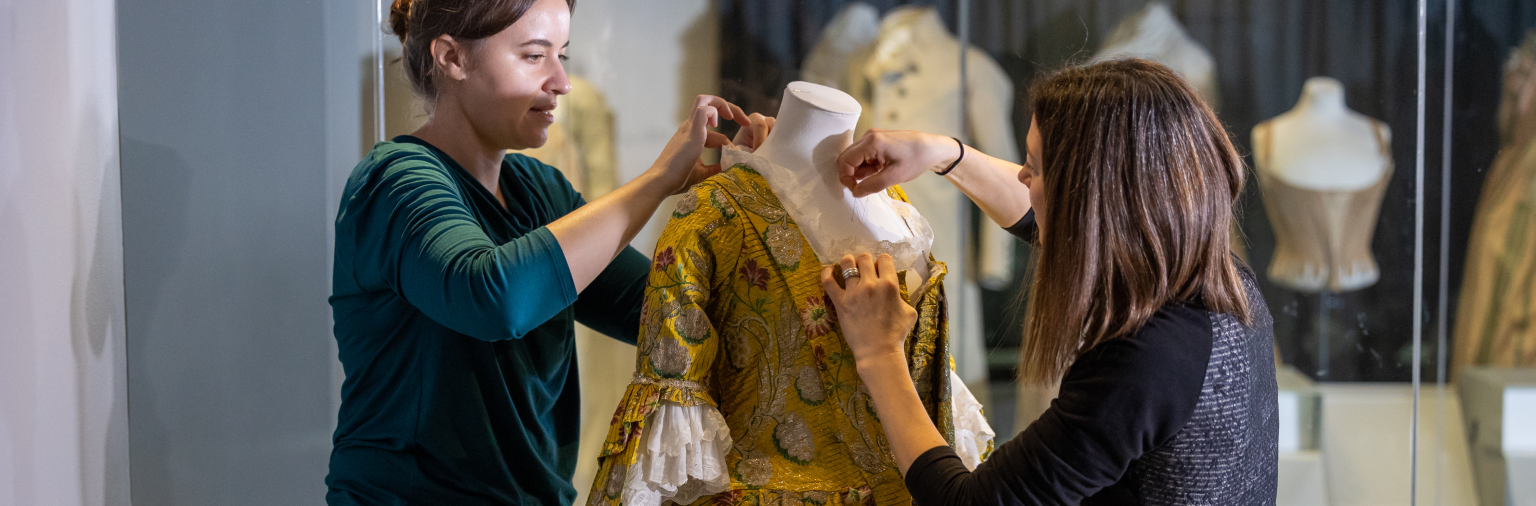 Two members of the collection team dress a mannequin